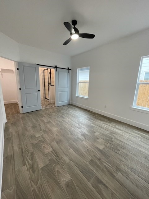 unfurnished bedroom featuring hardwood / wood-style flooring, a barn door, and ceiling fan