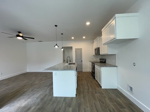 kitchen featuring stainless steel range with electric stovetop, hanging light fixtures, a kitchen island with sink, light stone counters, and white cabinets