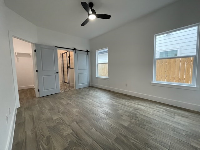 unfurnished bedroom featuring light wood-type flooring, a barn door, ceiling fan, and a walk in closet