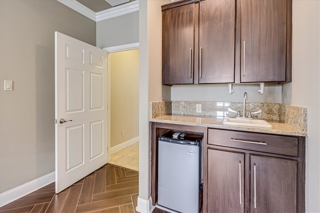 kitchen featuring light stone counters, dark brown cabinetry, sink, crown molding, and dark parquet flooring