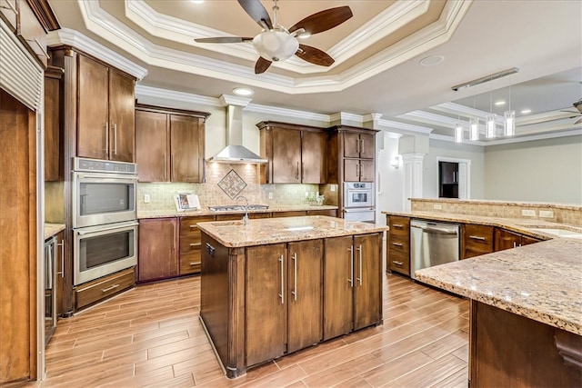 kitchen with wall chimney range hood, a raised ceiling, ornamental molding, and stainless steel appliances