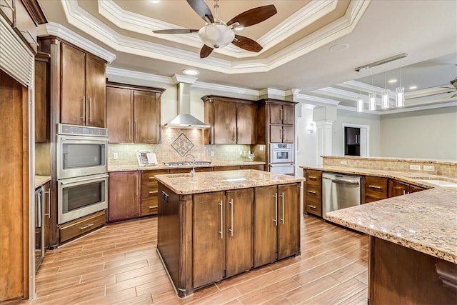 113 Bay Ct, Aransas Pass, TX 78336 - kitchen featuring stainless steel appliances, wall chimney exhaust hood, a raised ceiling, a center island with sink, and crown molding