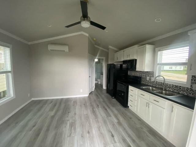 kitchen with sink, a wall mounted air conditioner, light hardwood / wood-style floors, white cabinets, and black appliances