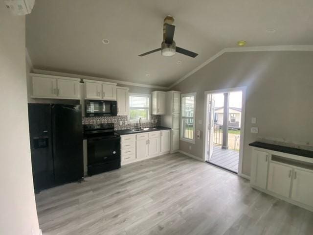 kitchen featuring white cabinets, black appliances, vaulted ceiling, and light wood-type flooring