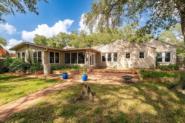 back of property featuring a sunroom, a lawn, and a fire pit