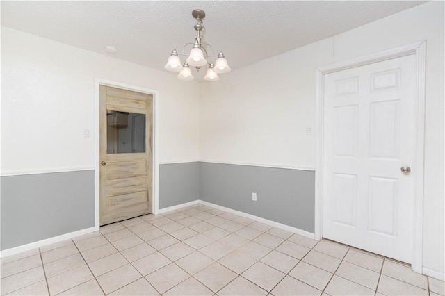 unfurnished room with an inviting chandelier, a textured ceiling, and light tile patterned flooring