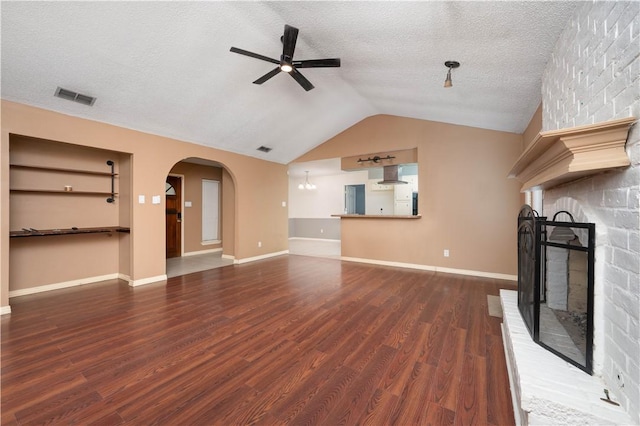 unfurnished living room featuring vaulted ceiling, a textured ceiling, dark hardwood / wood-style floors, a fireplace, and ceiling fan with notable chandelier