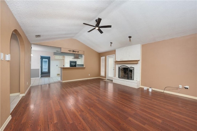 unfurnished living room featuring ceiling fan, hardwood / wood-style floors, a fireplace, a textured ceiling, and vaulted ceiling