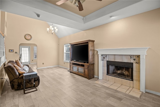 living room featuring a tiled fireplace, crown molding, vaulted ceiling, and ceiling fan with notable chandelier