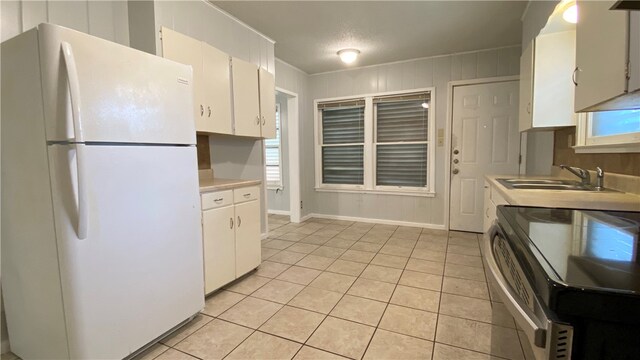 kitchen featuring light tile patterned flooring, white fridge, range with electric cooktop, sink, and white cabinets