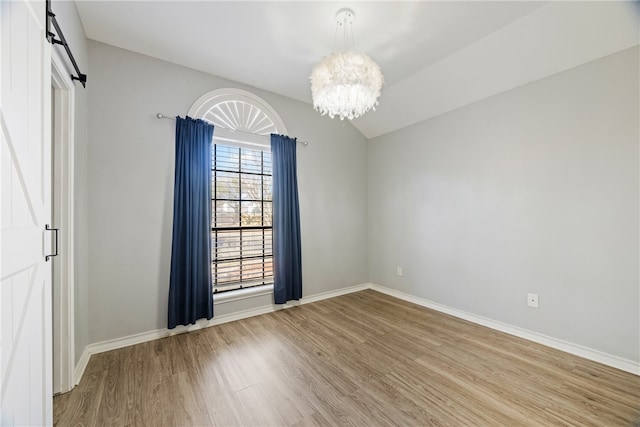 spare room featuring light hardwood / wood-style floors, a barn door, and a chandelier