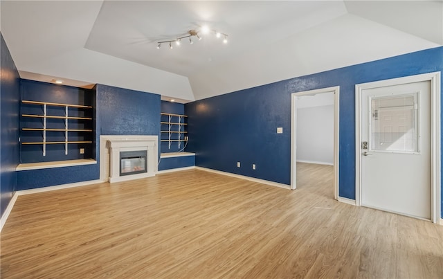 unfurnished living room featuring wood-type flooring, lofted ceiling, a large fireplace, and built in shelves