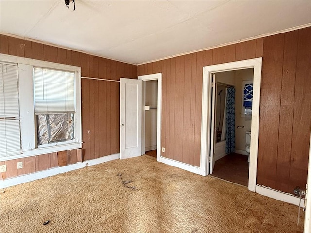 unfurnished bedroom featuring carpet floors, wooden walls, and ensuite bath