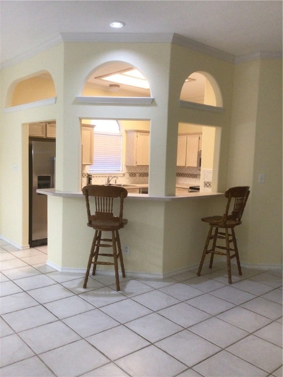 kitchen with tasteful backsplash, stainless steel appliances, light brown cabinets, a breakfast bar area, and kitchen peninsula