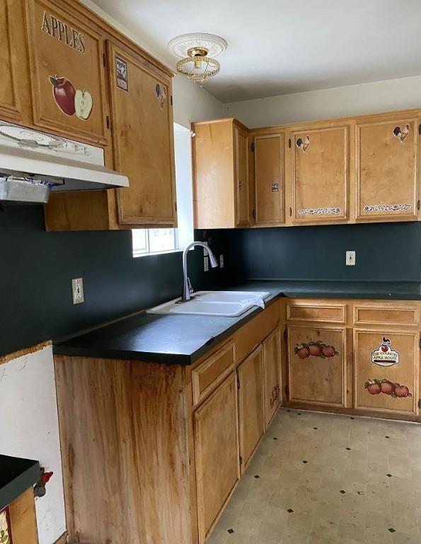 kitchen with light floors, a sink, under cabinet range hood, dark countertops, and brown cabinets