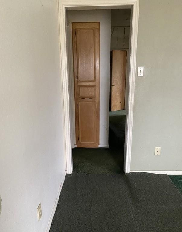 corridor featuring baseboards and dark carpet