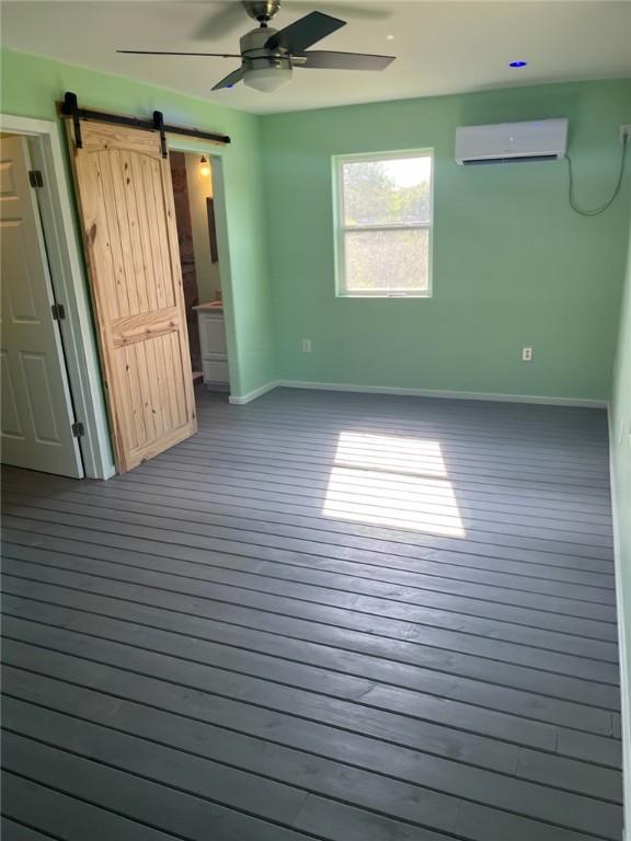 1123 S Fuqua St, Rockport, TX 78382 - unfurnished bedroom featuring a wall mounted air conditioner, baseboards, a barn door, wood finished floors, and a ceiling fan