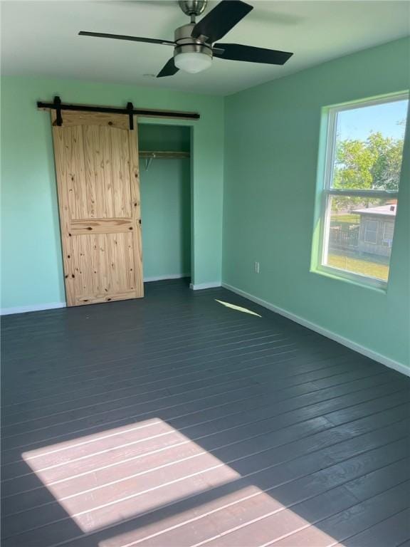 1123 S Fuqua St, Rockport, TX 78382 - unfurnished bedroom with baseboards, a barn door, dark wood-style flooring, and ceiling fan