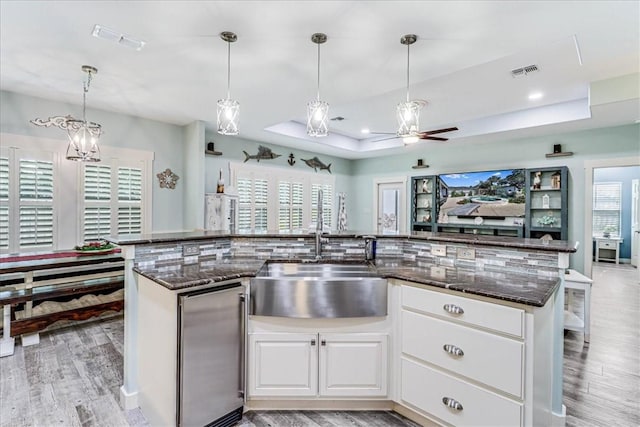 kitchen featuring sink, light hardwood / wood-style flooring, dark stone counters, a tray ceiling, and white cabinets