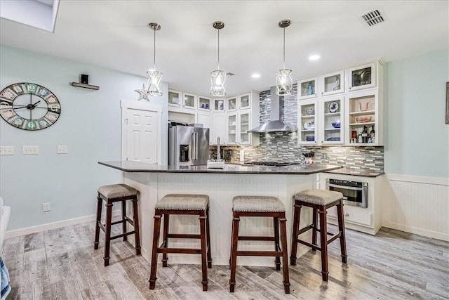 kitchen featuring white cabinets, wall chimney exhaust hood, stainless steel appliances, and decorative light fixtures