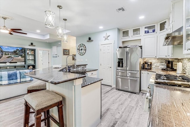 kitchen with dark stone countertops, decorative light fixtures, high quality fridge, white cabinets, and exhaust hood