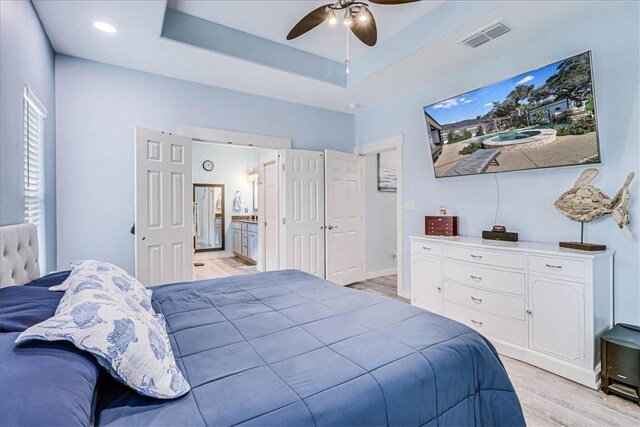 bedroom with a tray ceiling, connected bathroom, ceiling fan, and light hardwood / wood-style floors