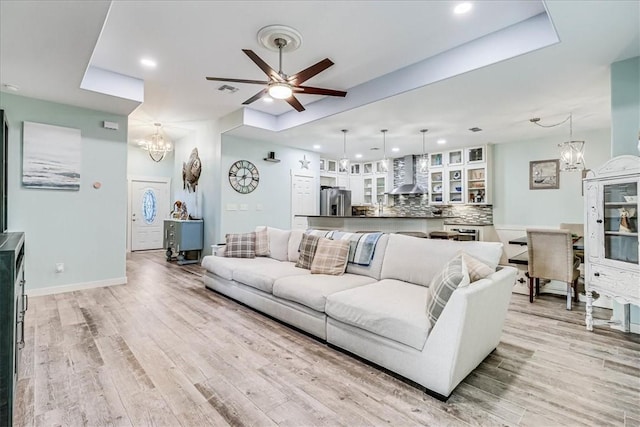 living room with a raised ceiling, light hardwood / wood-style flooring, and ceiling fan with notable chandelier