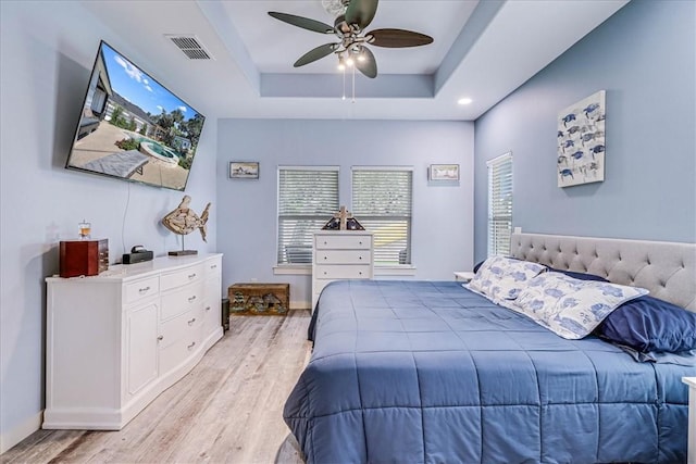 bedroom with a raised ceiling, ceiling fan, and light hardwood / wood-style floors