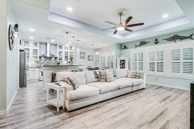 living room featuring light wood-type flooring, a tray ceiling, and ceiling fan