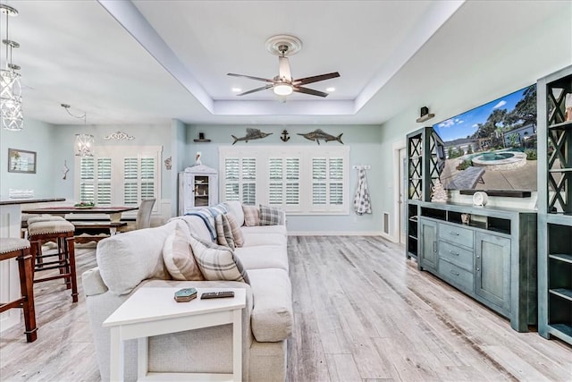 living room with ceiling fan with notable chandelier, light wood-type flooring, and a raised ceiling