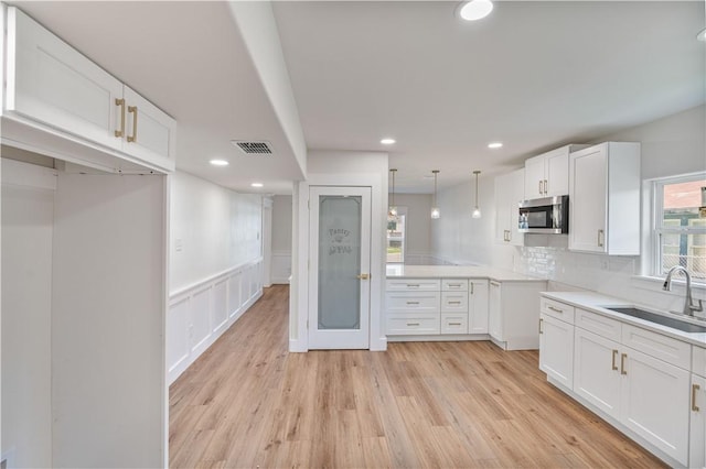 1101 6th St, Corpus Christi, TX 78404 - kitchen with stainless steel microwave, white cabinets, light wood finished floors, tasteful backsplash, and recessed lighting