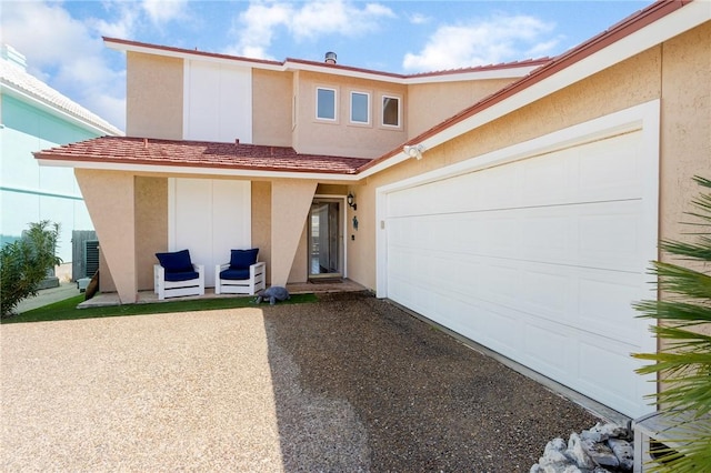 view of front facade with driveway, central AC unit, a tiled roof, an attached garage, and stucco siding