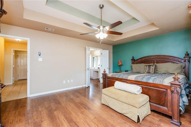 bedroom featuring visible vents, wood finished floors, baseboards, a raised ceiling, and ceiling fan