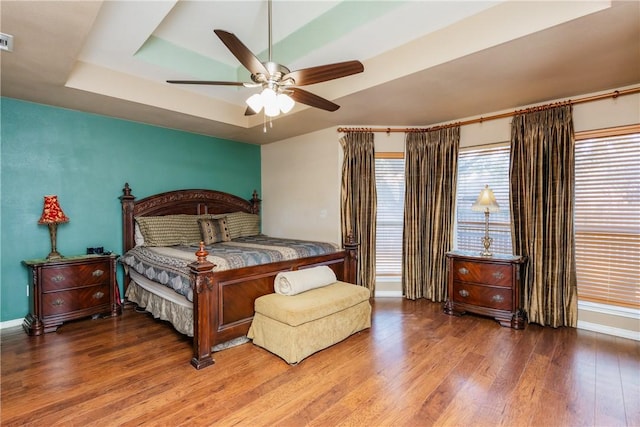 bedroom with a tray ceiling, baseboards, visible vents, and wood finished floors