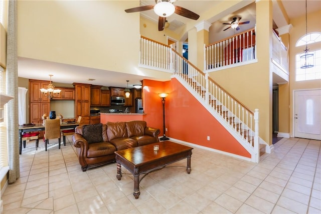 living room featuring stairway, baseboards, light tile patterned flooring, a towering ceiling, and ceiling fan with notable chandelier