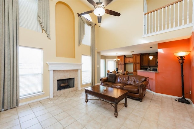 living area featuring a tiled fireplace, ceiling fan with notable chandelier, baseboards, and a towering ceiling