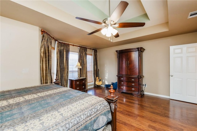 bedroom with a ceiling fan, wood finished floors, baseboards, visible vents, and a tray ceiling