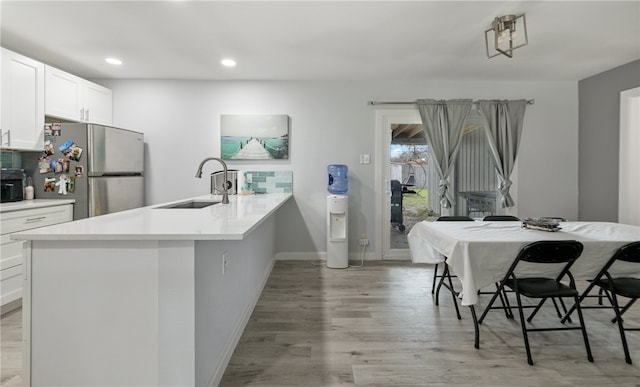 kitchen with light wood-type flooring, a breakfast bar, sink, white cabinetry, and stainless steel refrigerator