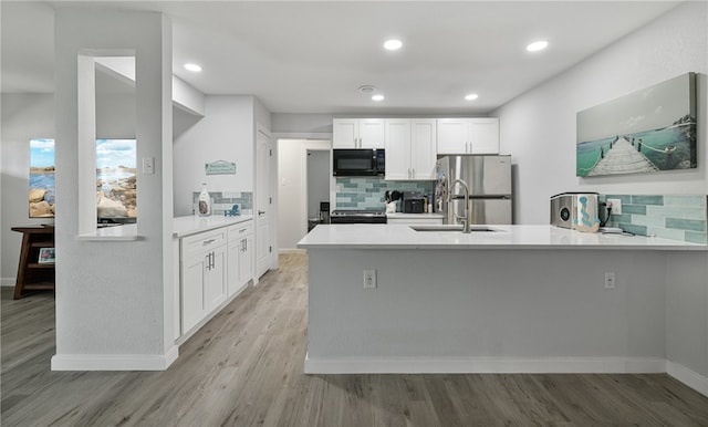 kitchen with white cabinets, appliances with stainless steel finishes, backsplash, and light hardwood / wood-style flooring