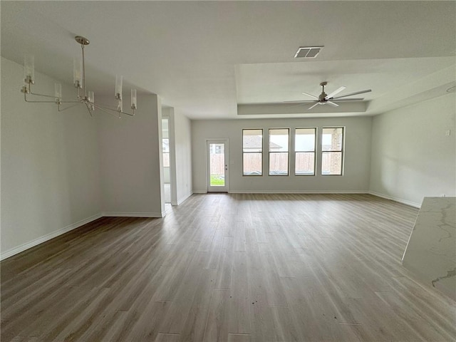 unfurnished living room with a tray ceiling, wood-type flooring, and ceiling fan with notable chandelier