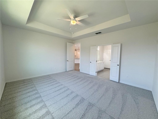 2550 Las Estrellas St, Corpus Christi, TX 78414 - unfurnished bedroom with a tray ceiling, light colored carpet, baseboards, ensuite bathroom, and a ceiling fan