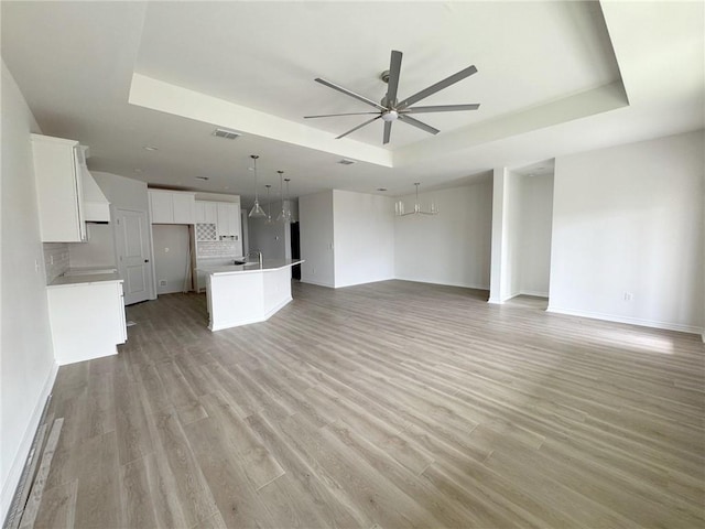 unfurnished living room with sink, a tray ceiling, and ceiling fan with notable chandelier