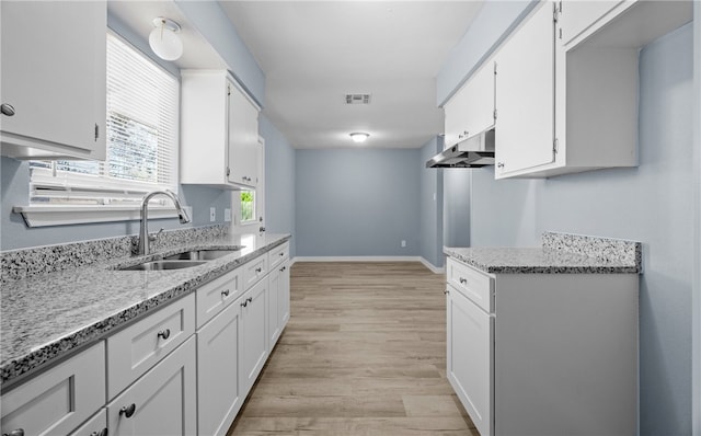 kitchen with light stone counters, visible vents, white cabinetry, and a sink