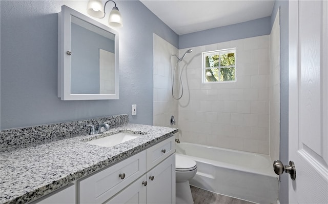 bathroom with toilet, wood finished floors, bathtub / shower combination, vanity, and a textured wall