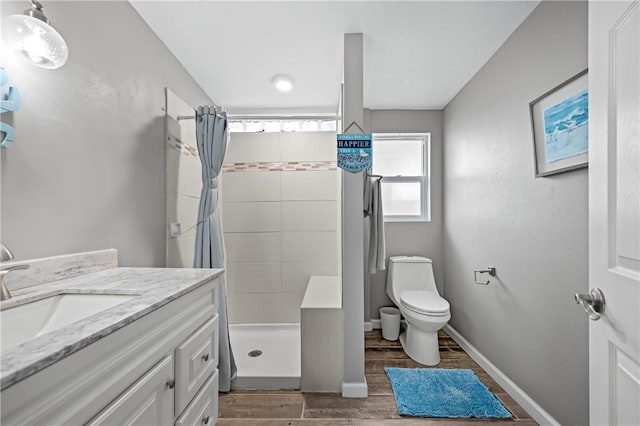 bathroom featuring wood finish floors, toilet, a stall shower, vanity, and baseboards