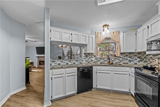 kitchen with a sink, light wood-type flooring, black appliances, white cabinetry, and backsplash