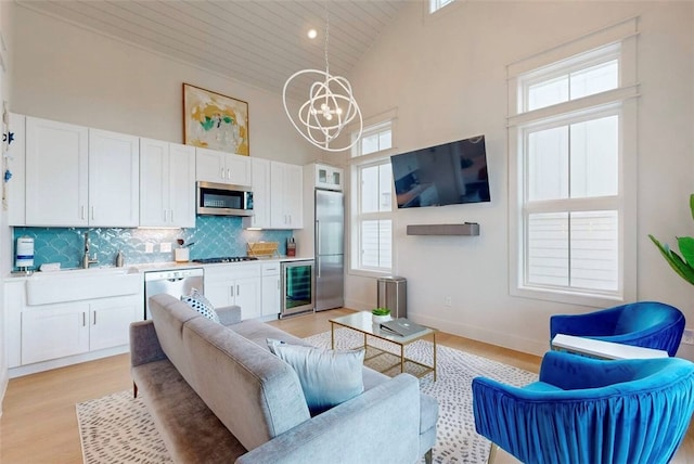 living room with light hardwood / wood-style floors, a chandelier, sink, high vaulted ceiling, and wine cooler