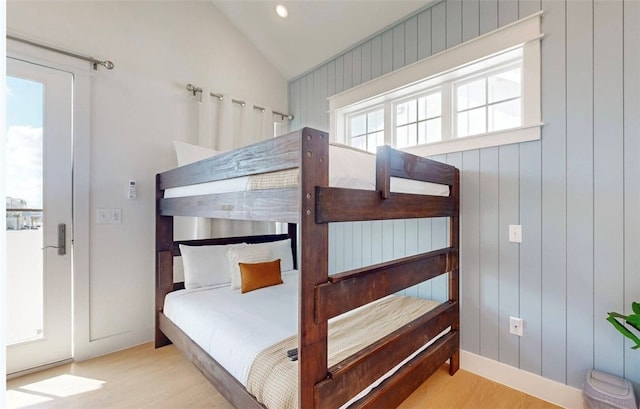 bedroom with light wood-type flooring, wood walls, and vaulted ceiling