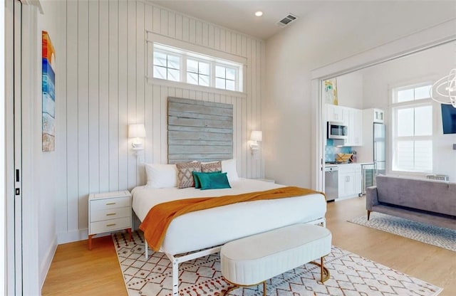 bedroom featuring wood walls, wood-type flooring, multiple windows, and stainless steel refrigerator