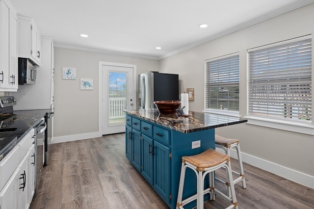 kitchen featuring a breakfast bar, white cabinets, blue cabinets, dark stone countertops, and stainless steel appliances